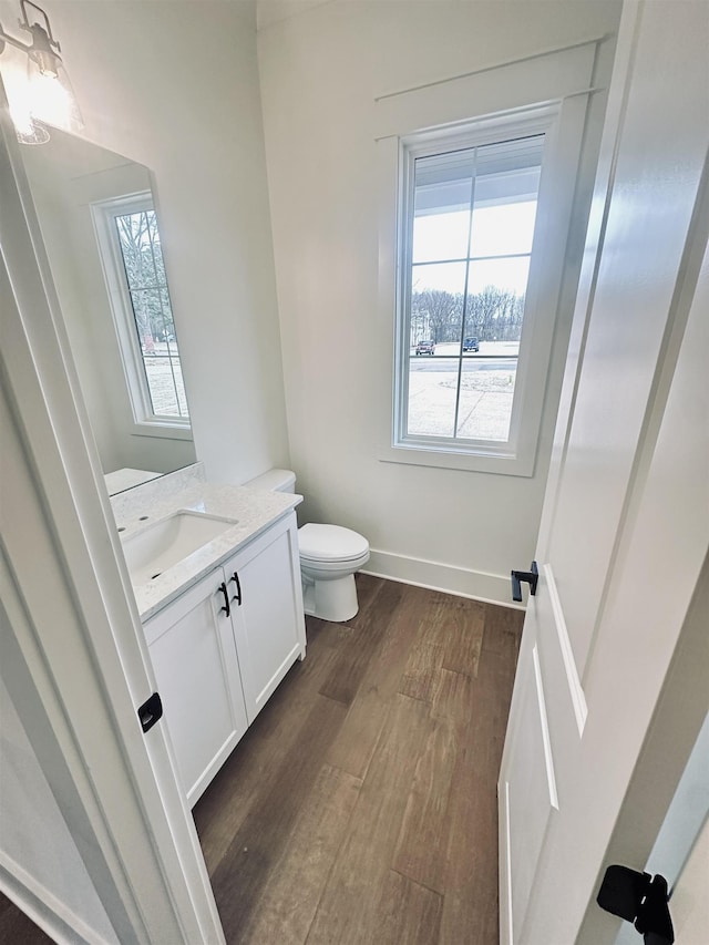 half bath featuring vanity, toilet, wood finished floors, and a wealth of natural light