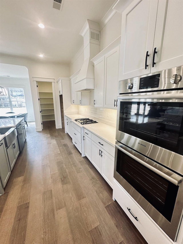 kitchen featuring visible vents, backsplash, double oven, custom range hood, and gas stovetop