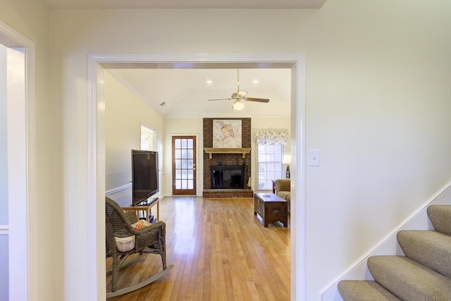 living room with ceiling fan, lofted ceiling, stairs, a brick fireplace, and light wood finished floors