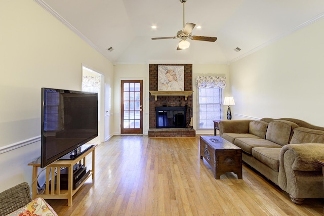 living room featuring a fireplace, a ceiling fan, visible vents, light wood-style floors, and crown molding