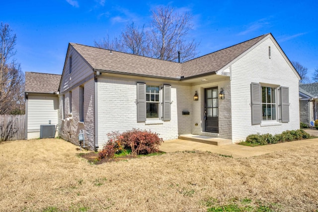 ranch-style home with a shingled roof, a front lawn, cooling unit, and brick siding