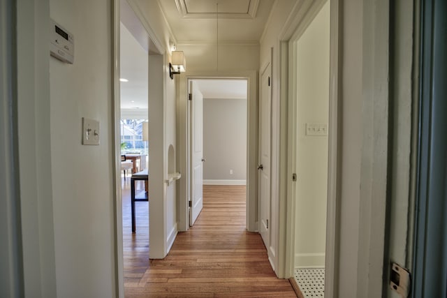 hall featuring attic access, crown molding, baseboards, and wood finished floors