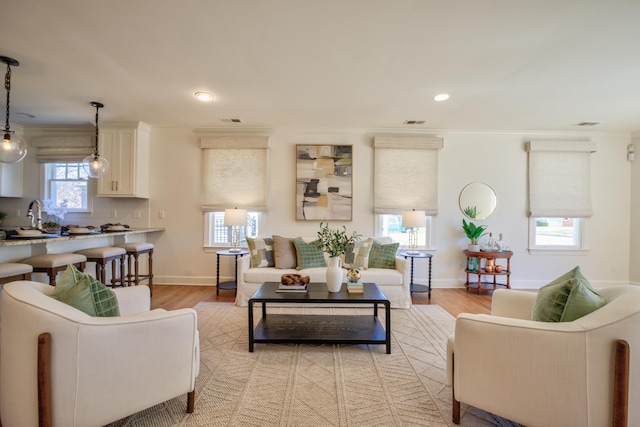 living area featuring baseboards, crown molding, visible vents, and light wood-style floors