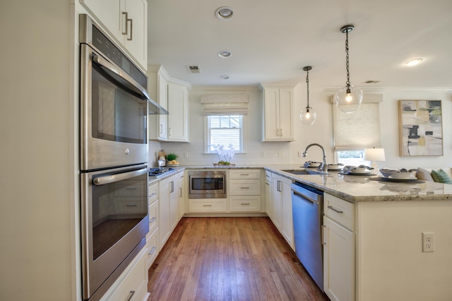 kitchen featuring visible vents, appliances with stainless steel finishes, a sink, light stone countertops, and a peninsula