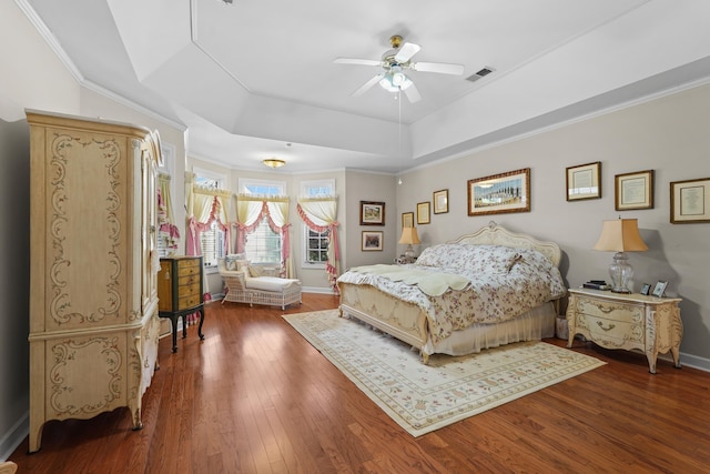 bedroom featuring baseboards, visible vents, a raised ceiling, hardwood / wood-style flooring, and crown molding