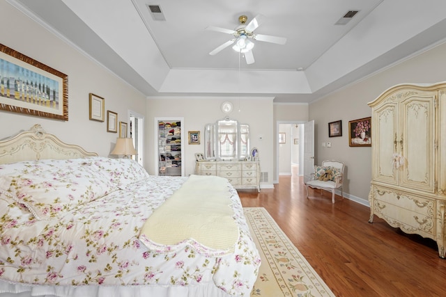 bedroom with wood finished floors, a raised ceiling, visible vents, and a walk in closet