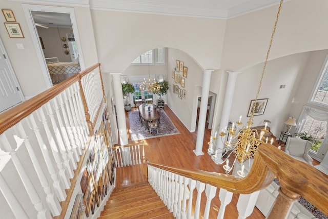 stairway with a chandelier, wood finished floors, a towering ceiling, a healthy amount of sunlight, and decorative columns