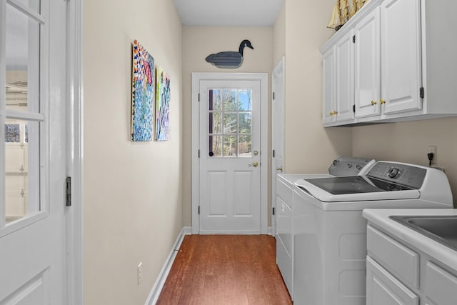 clothes washing area with dark wood-style flooring, washing machine and dryer, cabinet space, and baseboards