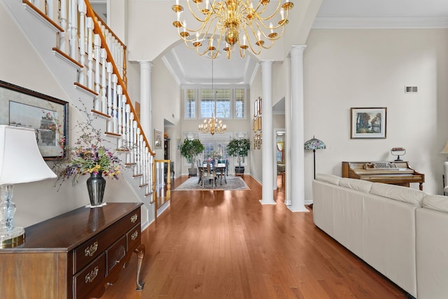 entryway with decorative columns, ornamental molding, wood finished floors, stairs, and a chandelier