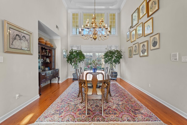 dining room with baseboards, visible vents, wood finished floors, crown molding, and a notable chandelier