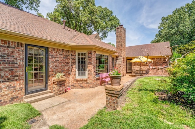 rear view of property with a patio, brick siding, a chimney, and a shingled roof