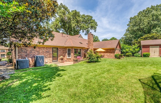 rear view of property with central air condition unit, a yard, a chimney, and brick siding