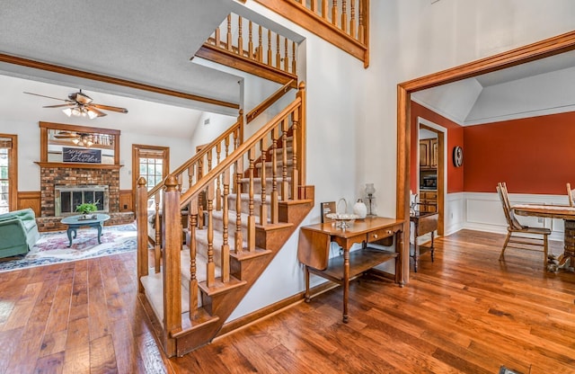 stairway featuring a ceiling fan, wainscoting, a fireplace, and hardwood / wood-style floors