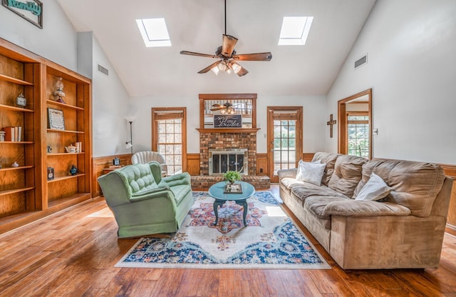 living room with a skylight, a brick fireplace, a wainscoted wall, and visible vents