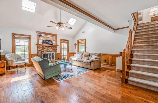 living room with a brick fireplace, a wainscoted wall, wood-type flooring, and stairs