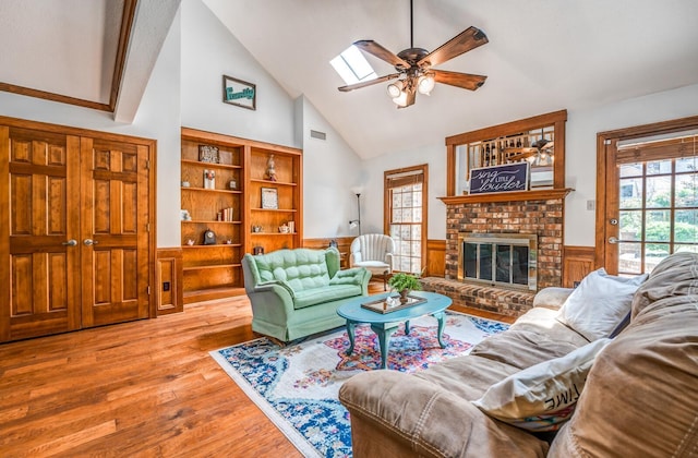 living room with a skylight, a wainscoted wall, ceiling fan, wood finished floors, and a fireplace