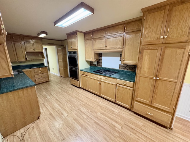 kitchen featuring dark countertops, black appliances, light wood finished floors, and a sink