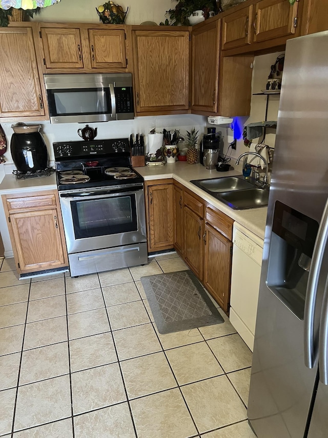 kitchen with light tile patterned floors, stainless steel appliances, light countertops, brown cabinetry, and a sink