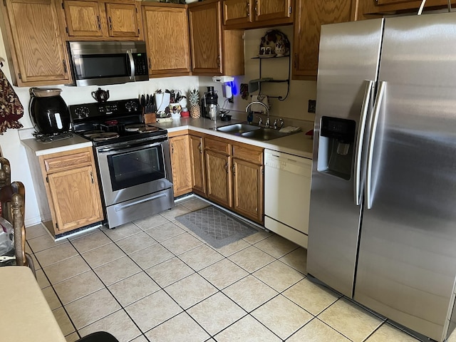 kitchen with appliances with stainless steel finishes, light countertops, a sink, and light tile patterned floors