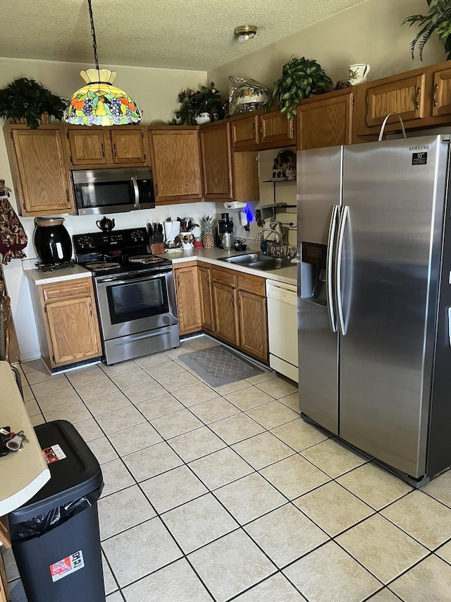 kitchen featuring a textured ceiling, a sink, light countertops, appliances with stainless steel finishes, and brown cabinets