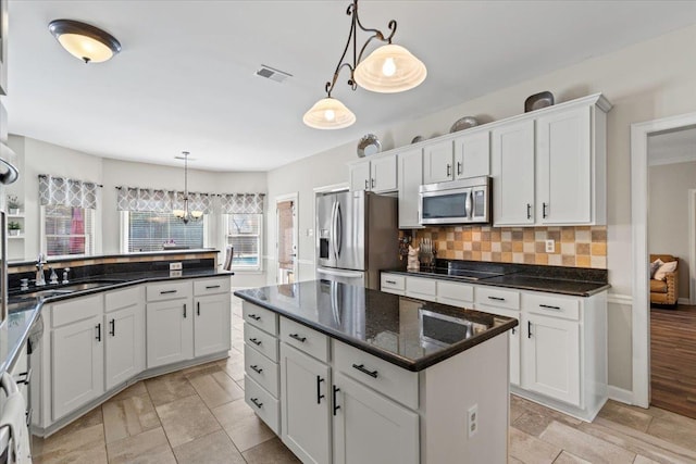 kitchen with stainless steel appliances, white cabinetry, a center island, tasteful backsplash, and decorative light fixtures