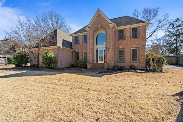 view of front of property featuring a front yard, brick siding, and roof with shingles