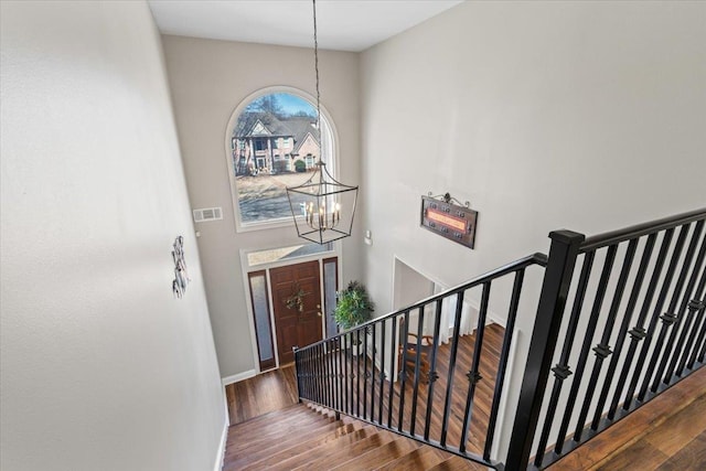 staircase with a notable chandelier, a high ceiling, wood finished floors, visible vents, and baseboards