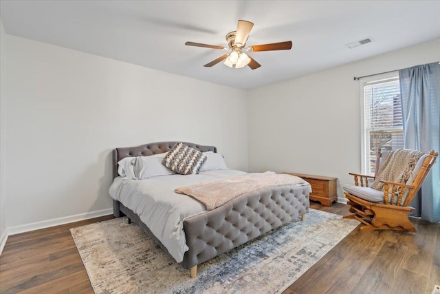 bedroom with a ceiling fan, visible vents, baseboards, and wood finished floors