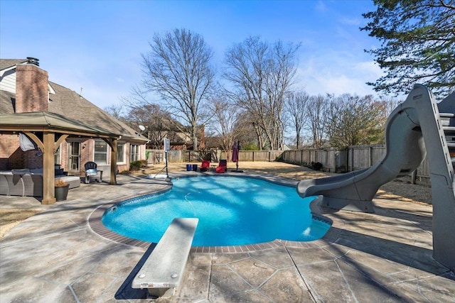 view of swimming pool with a patio, a water slide, a fenced backyard, an outdoor living space, and a diving board