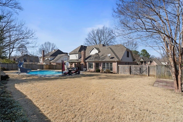 back of house featuring a fenced backyard, brick siding, a yard, a gate, and a fenced in pool