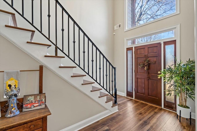 foyer entrance featuring visible vents, a towering ceiling, wood finished floors, baseboards, and stairs