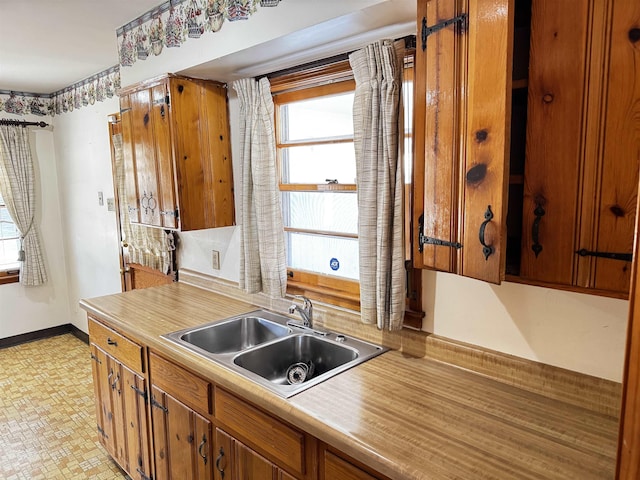 kitchen with brown cabinets, baseboards, light countertops, and a sink