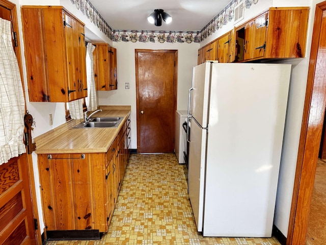 kitchen with light floors, light countertops, brown cabinetry, freestanding refrigerator, and a sink