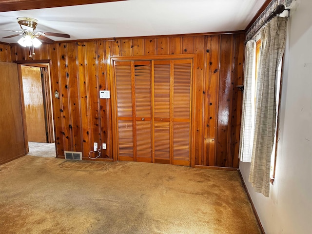 spare room featuring carpet floors, wooden walls, and visible vents