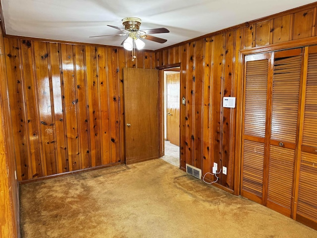 carpeted spare room with ornamental molding, visible vents, wood walls, and ceiling fan