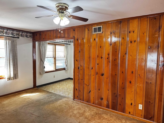 unfurnished room featuring ceiling fan, carpet floors, wood walls, visible vents, and baseboards