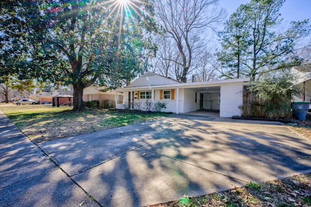 ranch-style home featuring brick siding, a porch, concrete driveway, a front yard, and a carport