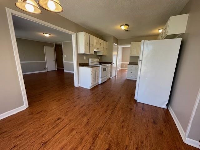 kitchen featuring dark wood finished floors, dark countertops, white cabinets, white appliances, and baseboards