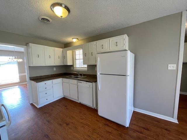 kitchen with white appliances, dark countertops, a sink, and visible vents