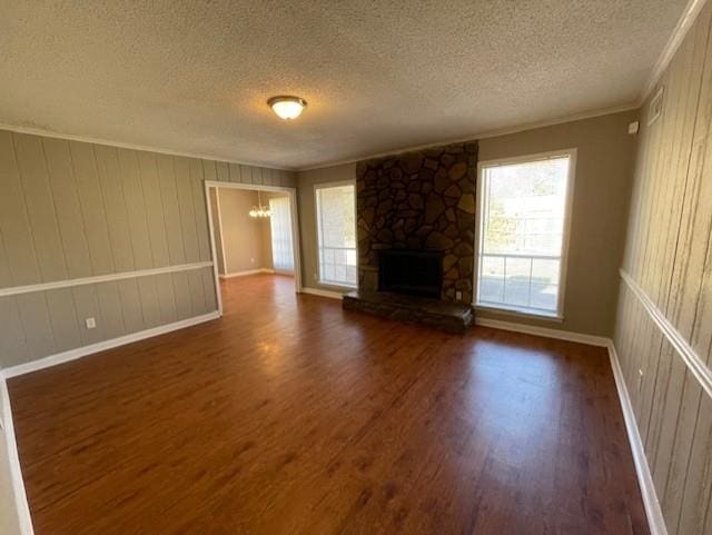 unfurnished living room featuring dark wood-style flooring, ornamental molding, a stone fireplace, a textured ceiling, and baseboards