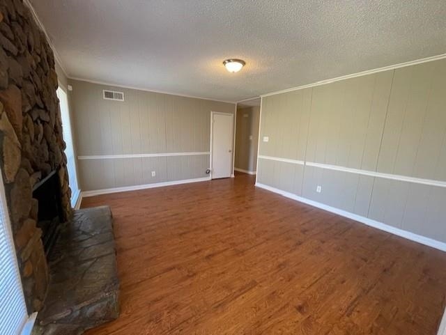 unfurnished living room featuring visible vents, ornamental molding, wood finished floors, a textured ceiling, and a stone fireplace