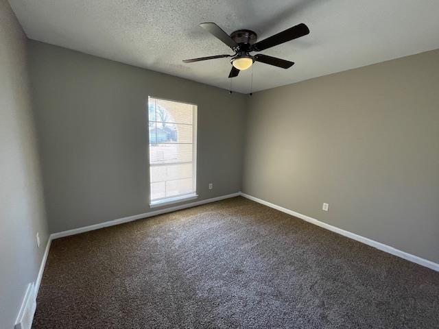 unfurnished room featuring a textured ceiling, dark colored carpet, ceiling fan, and baseboards