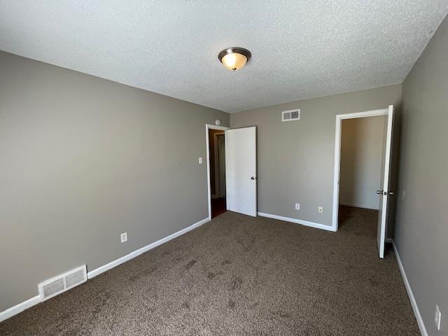 unfurnished bedroom with baseboards, visible vents, dark colored carpet, and a textured ceiling