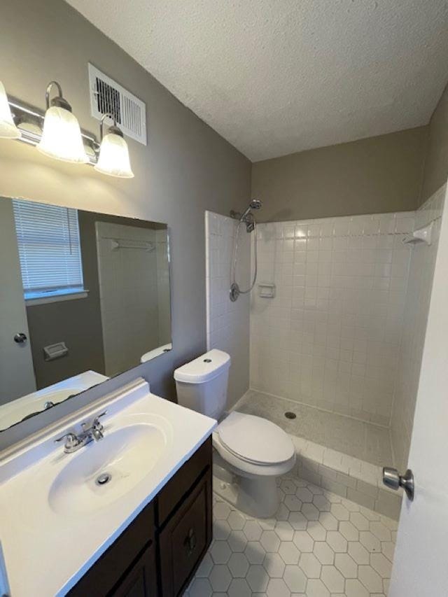 bathroom with toilet, visible vents, tiled shower, and vanity