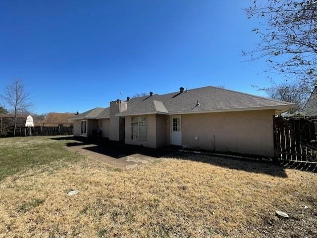 rear view of house featuring stucco siding, fence, and a yard