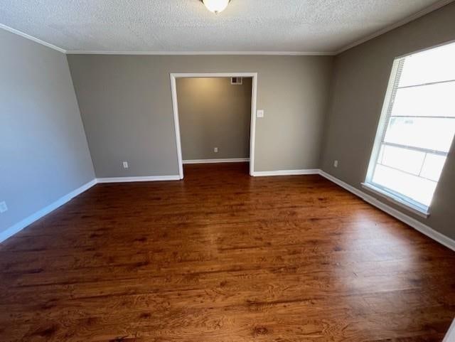 empty room featuring a textured ceiling, baseboards, dark wood-style flooring, and ornamental molding