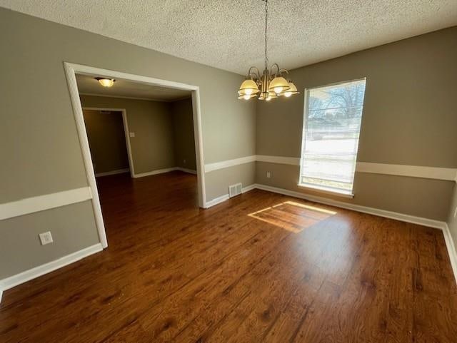 unfurnished room with a textured ceiling, a chandelier, and wood finished floors