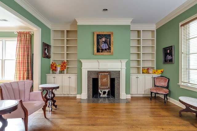 living area with ornamental molding, built in shelves, wood finished floors, and a high end fireplace