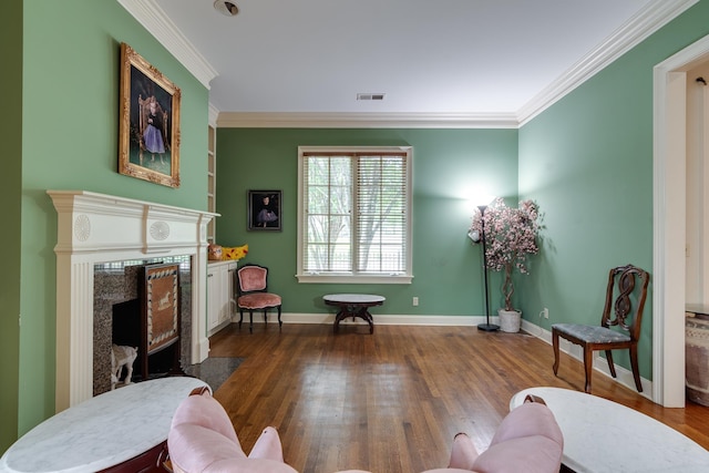 sitting room with a fireplace, visible vents, crown molding, and wood finished floors