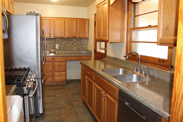 kitchen featuring brown cabinetry, dishwasher, decorative backsplash, gas range, and a sink